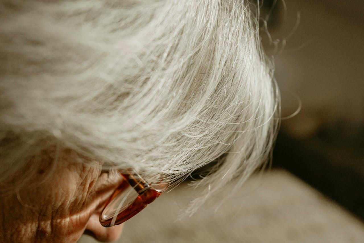 A calm, white-haired older adult wearing glasses, softly lit and looking content, after vision has been restored