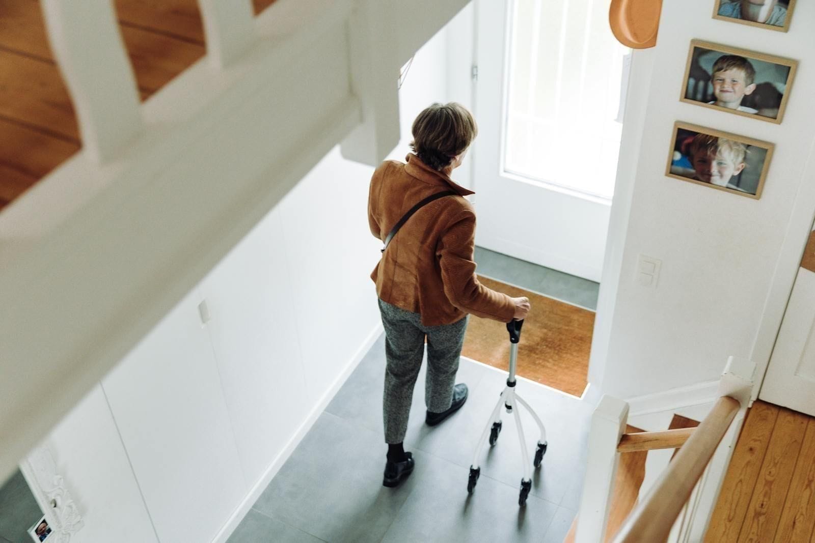 An older adult in a quiet, modern hallway taking careful, measured steps with a four-wheeled rollator walker, the slow deliberate posture of someone in the middle weeks of recovery, learning again how a body moves when one joint is brand new