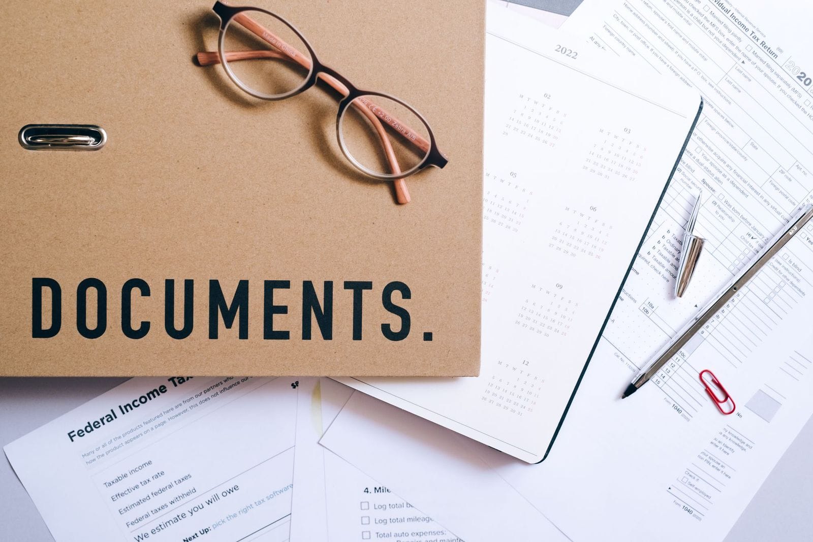 A flat lay of documents, a calendar, and reading glasses neatly arranged on a desk