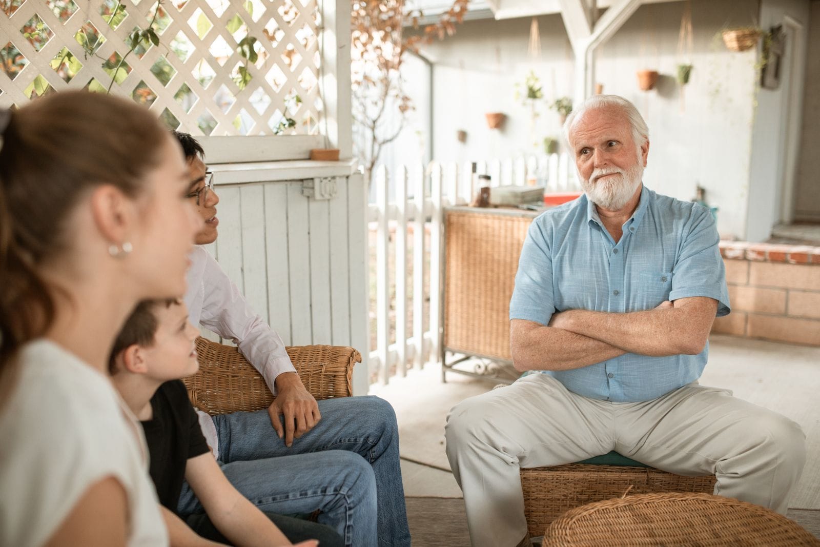An older man with a white beard listening attentively as his adult daughter and grandchild talk with him on a sunlit porch