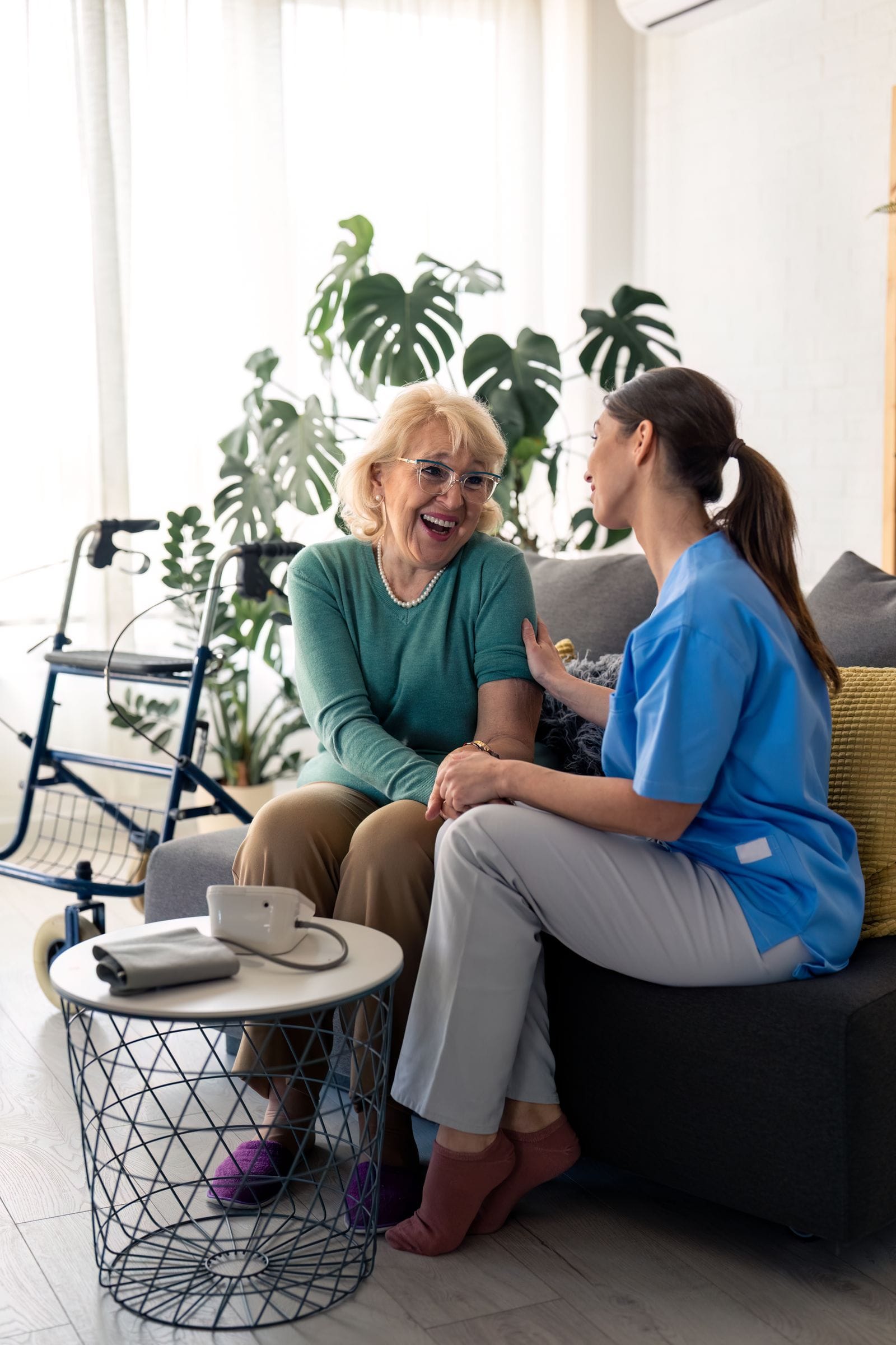 An older woman laughing and holding hands with her caregiver on the sofa