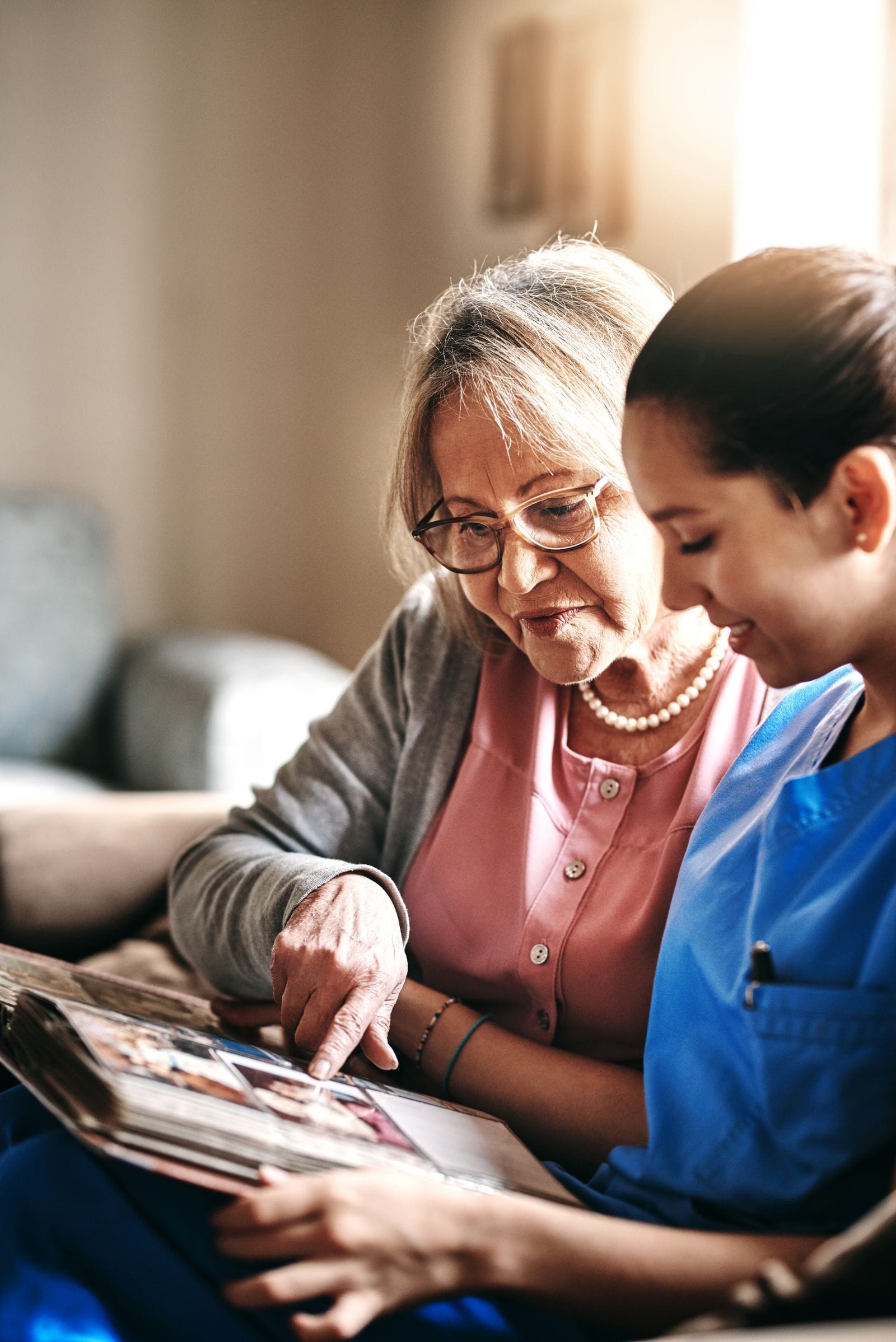 A nurse looking through a photo album with an older woman on the sofa