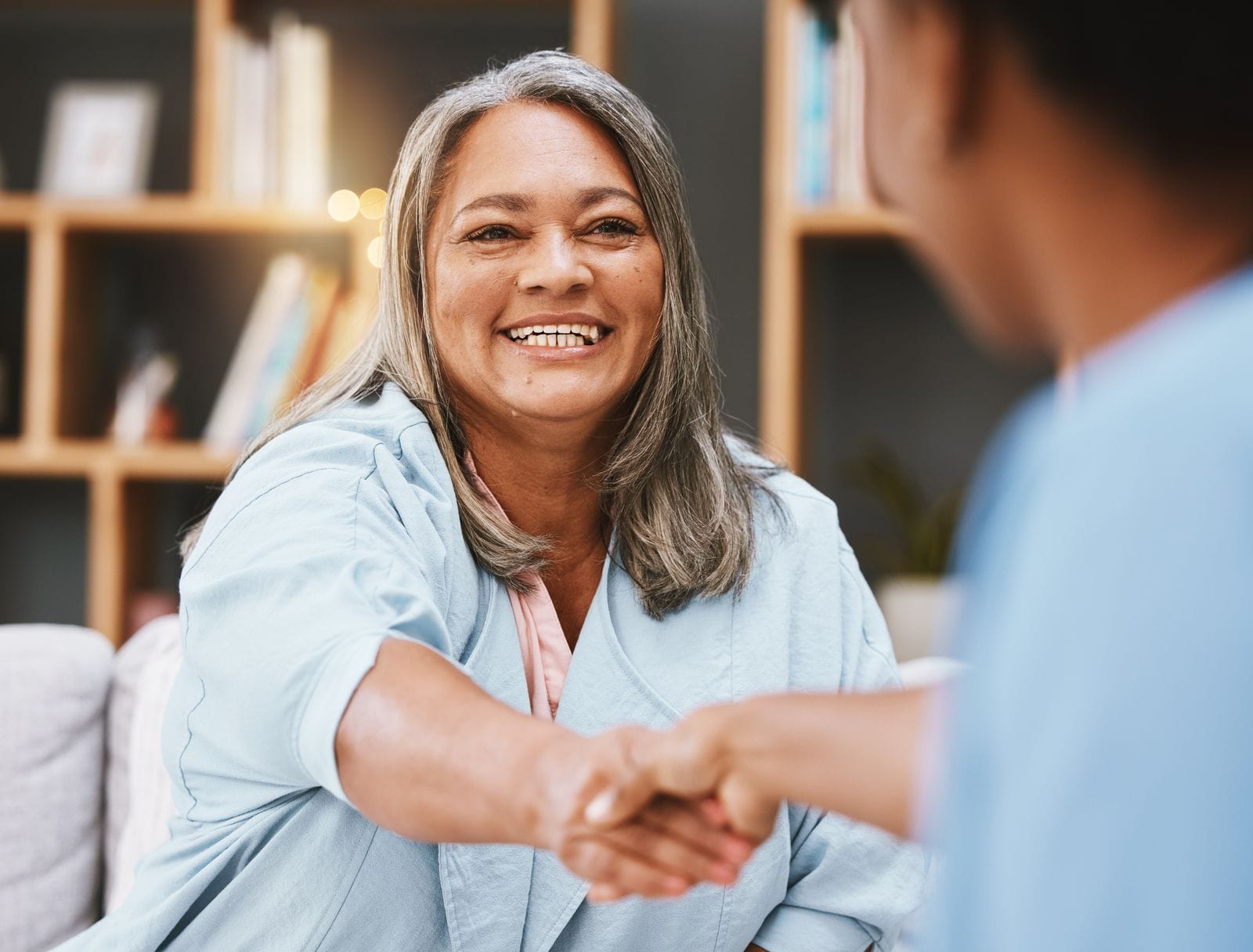 A smiling older woman shaking hands with a nurse in her living room